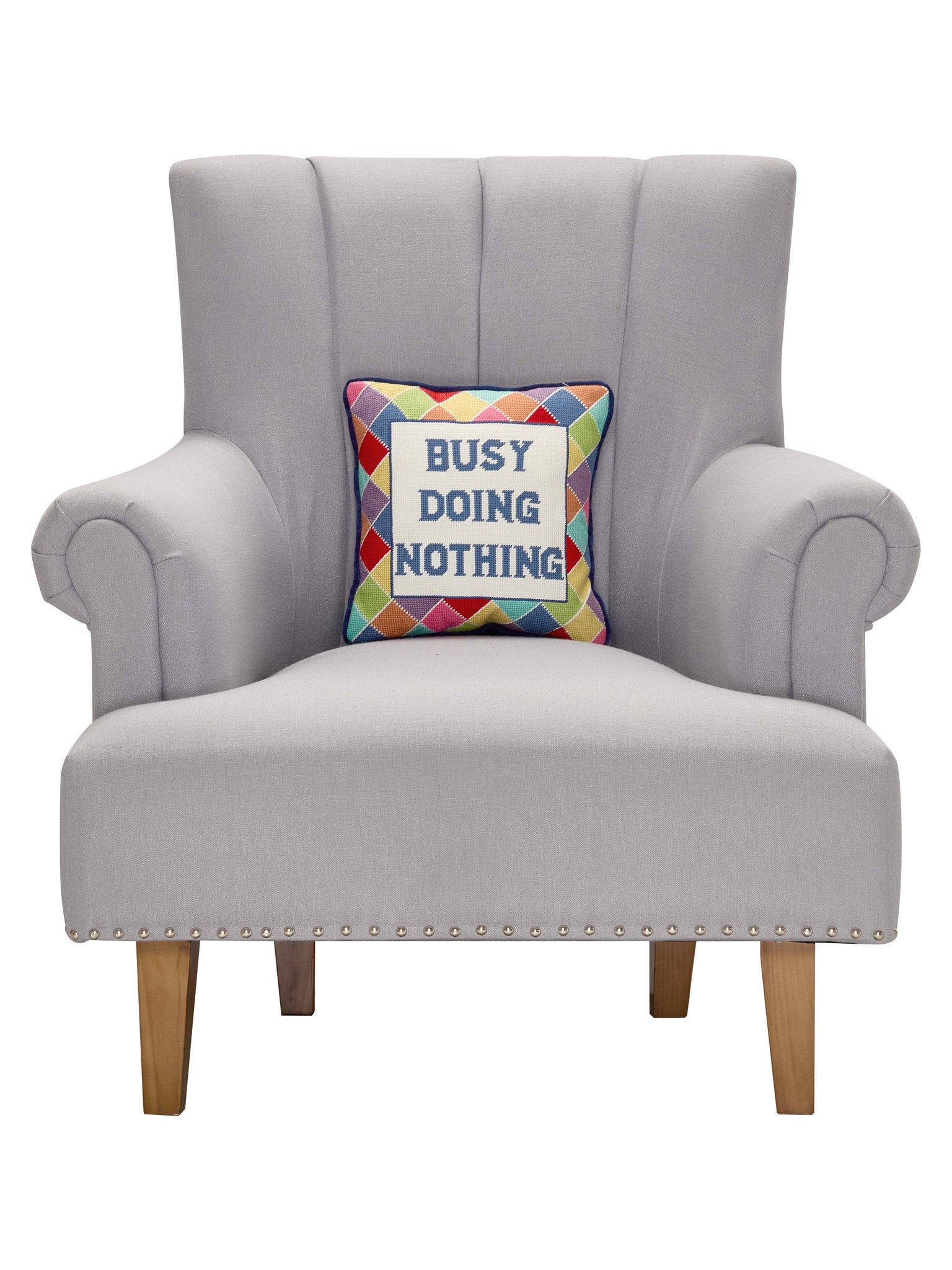 Busy Doing Nothing Embroidered Needlepoint Throw Pillow on an armchair, showing the throw pillow at room scale, 12x12 inch