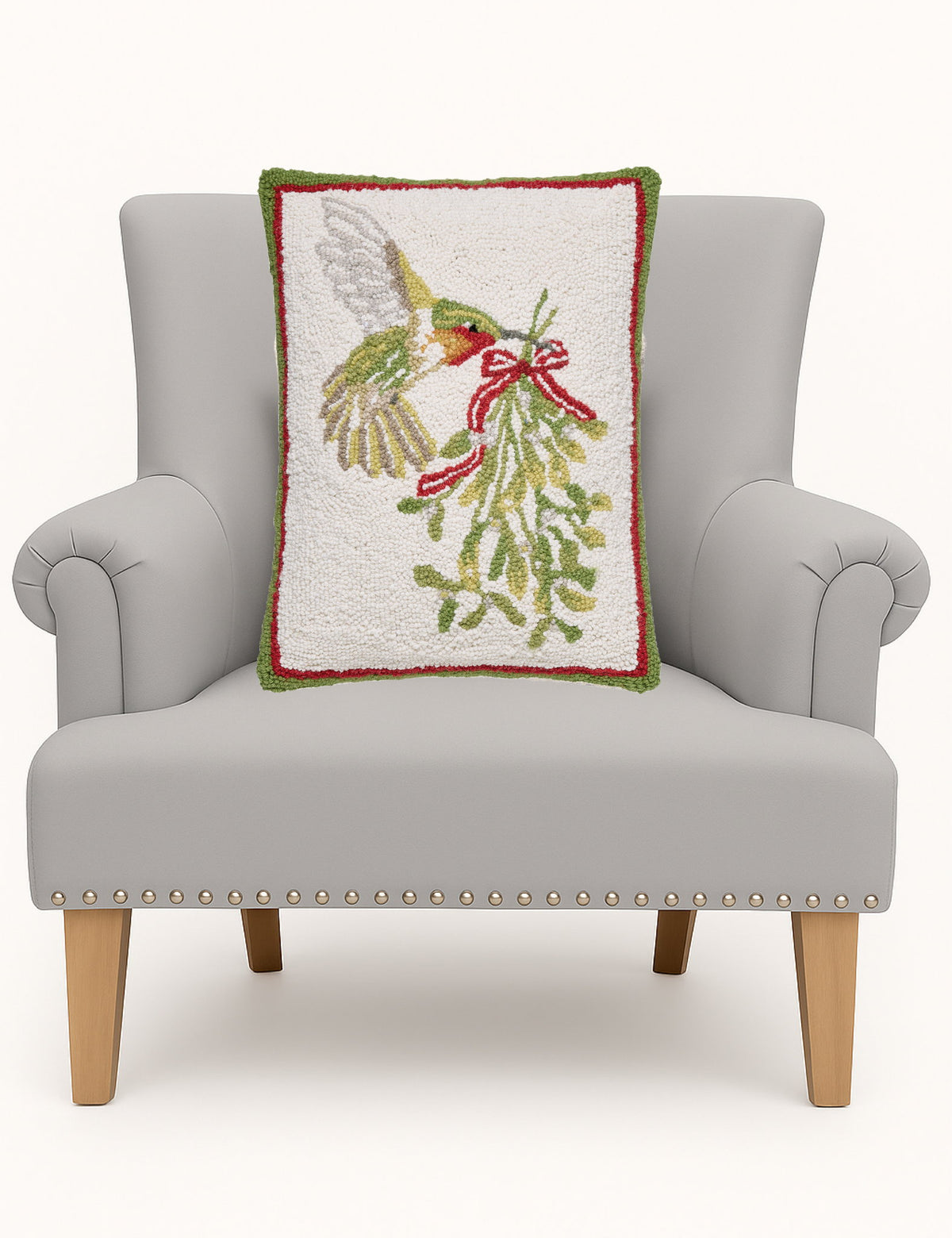 Hummingbird Mistletoe Hooked Wool Christmas Throw Pillow on an armchair, showing the throw pillow at room scale, 14x18 inch