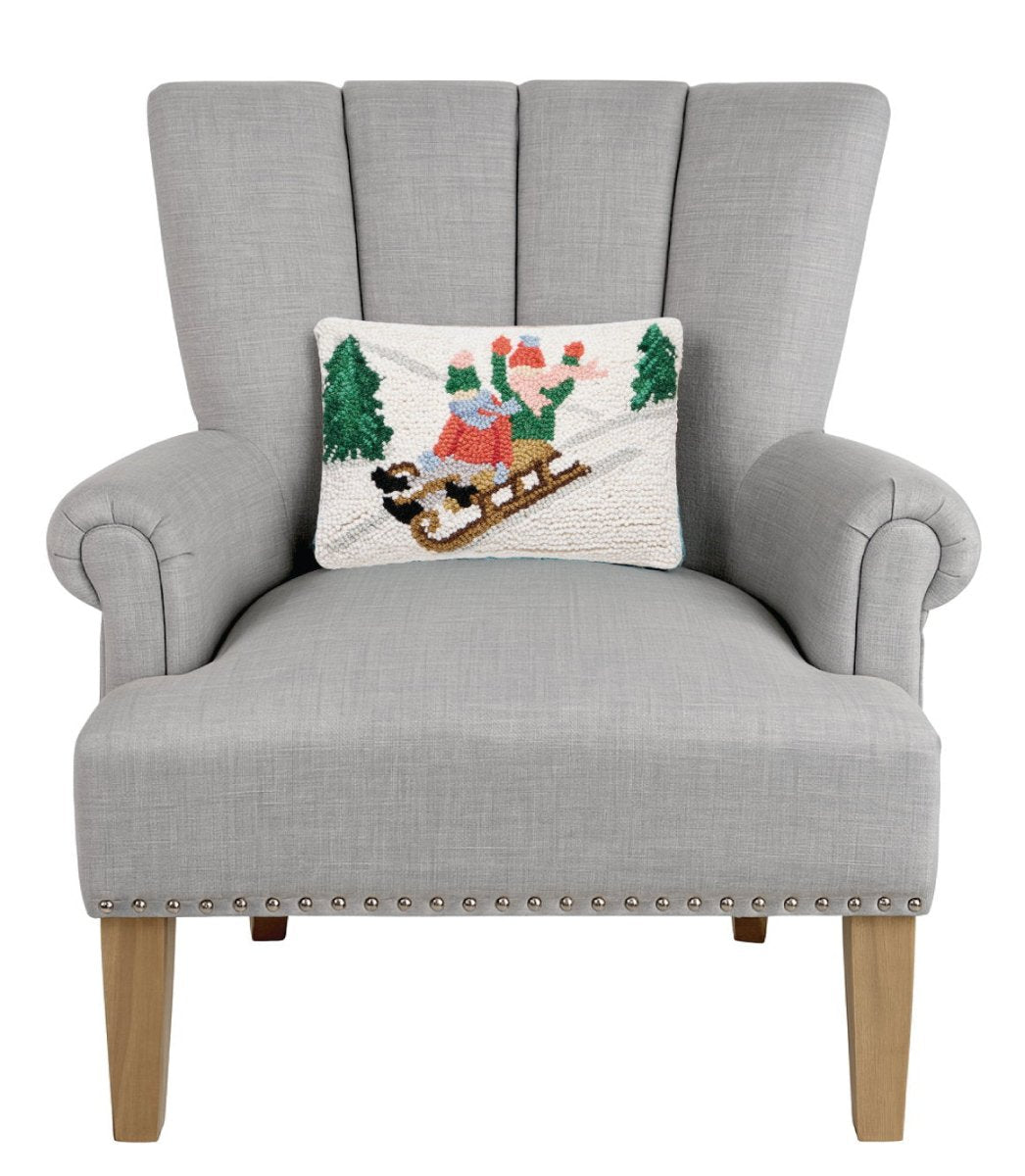Sledding Kids Hooked Wool Christmas Throw Pillow on an armchair, showing the throw pillow at room scale, 8x12 inch