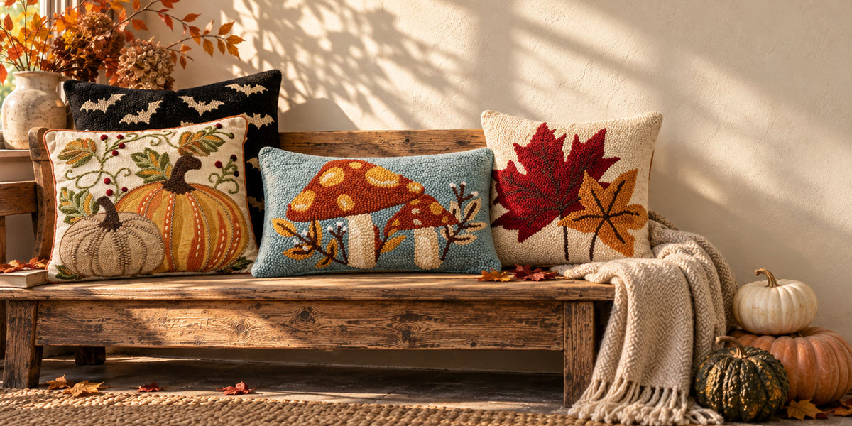 Hooked wool fall pillows with pumpkins, mushrooms, and autumn leaves styled on a rustic farmhouse bench