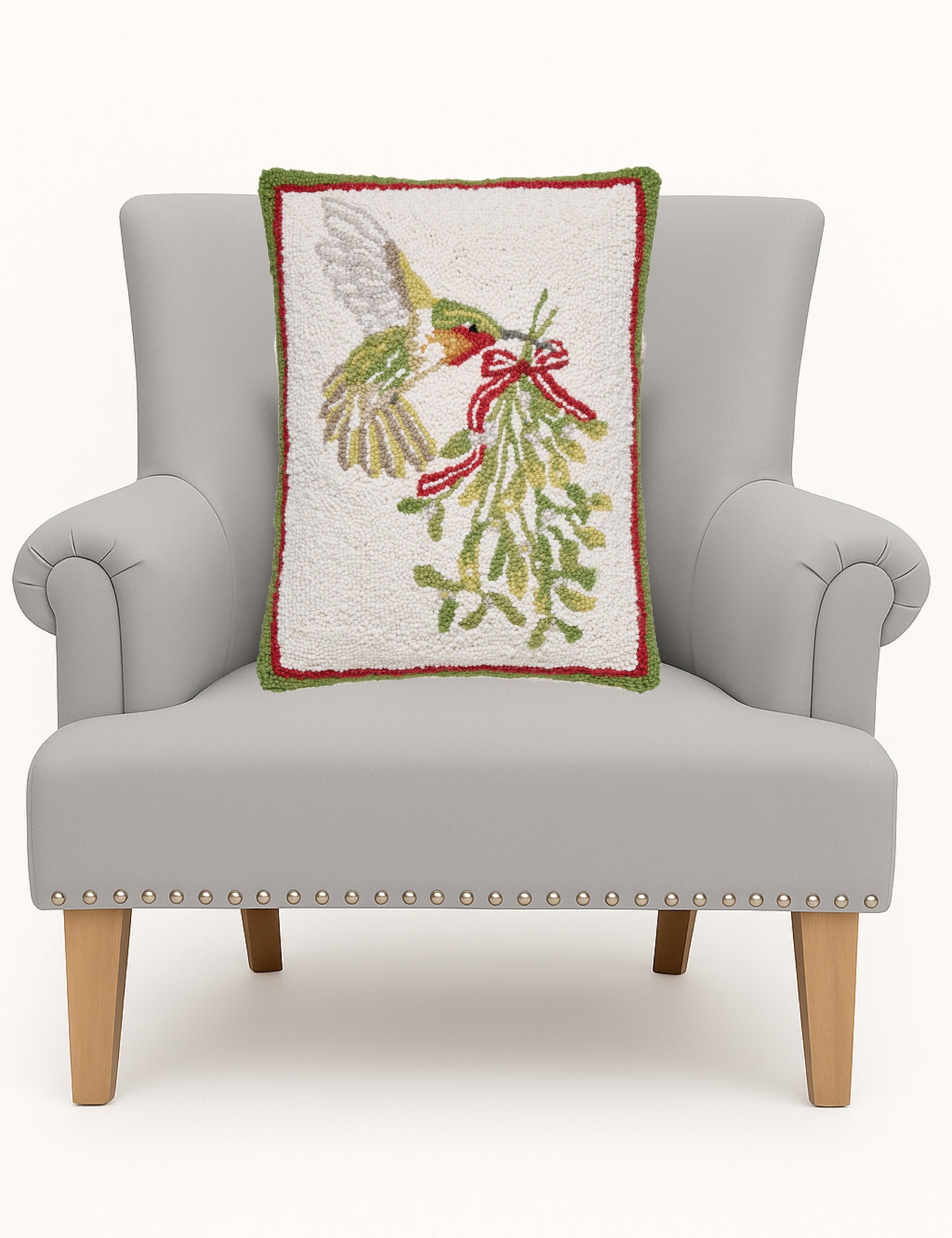 Hummingbird Mistletoe Hooked Wool Christmas Throw Pillow on an armchair, showing the throw pillow at room scale, 14x18 inch
