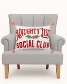 Naughty Social Club Embroidered Christmas Throw Pillow on an armchair, showing the throw pillow at room scale, 12x18 inch